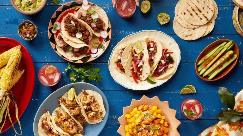 Bowls filled with taco dishes on table with corn and vegetable side dishes