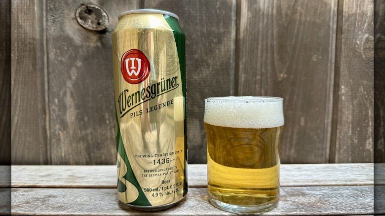 A can of Wernesgrüner Pilsner next to a glass of the beer