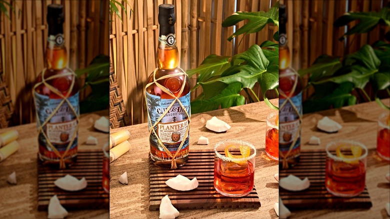Bottle and glass of Planteray Cut & Dry Coconut Rum surrounded by coconut pieces
