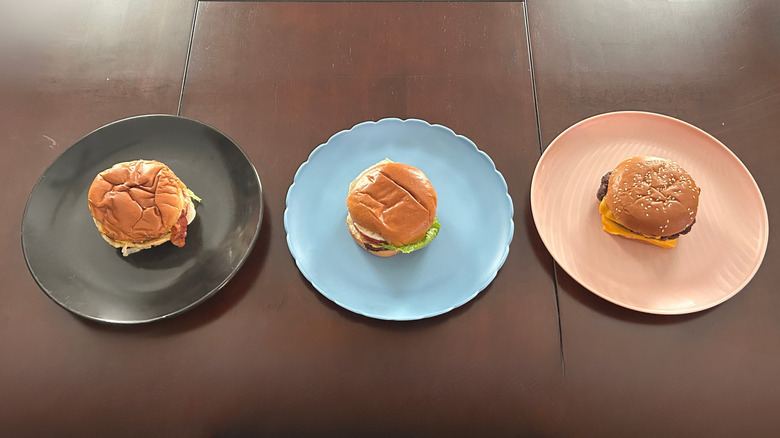 Three fast food bacon cheeseburgers on plates atop a wood table