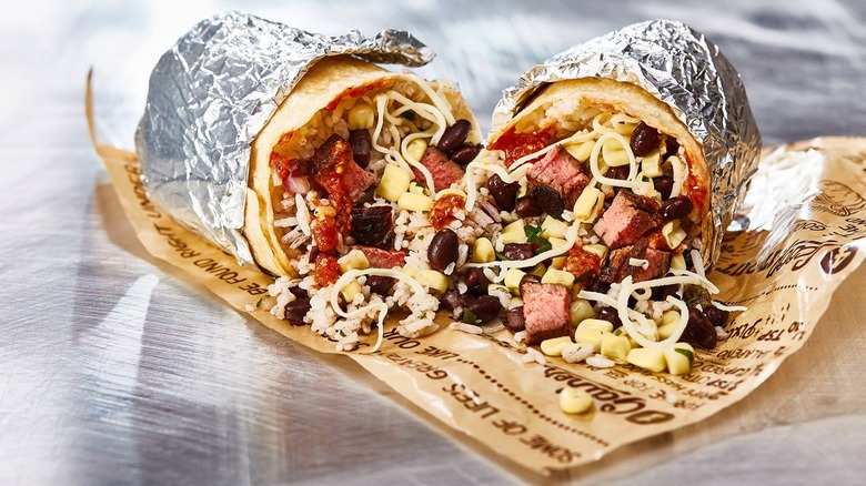 Chipotle burrito in foil on paper atop metal table