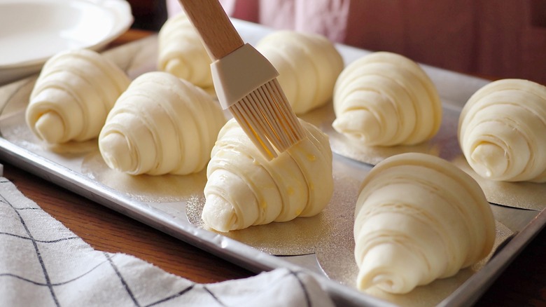 Egg wash being brushed onto a croissant 
