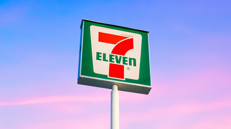 A 7-Eleven sign high up against a blue sky with pink clouds