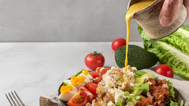 Hand pouring dressing onto salad