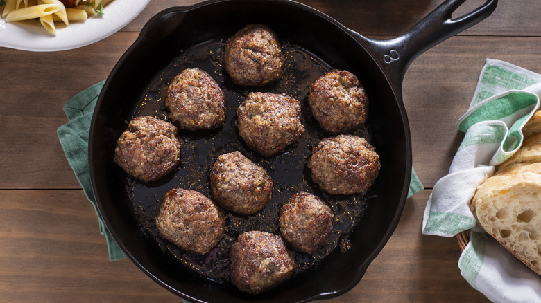 Cast iron skillet containing 10 Italian meatballs on green towel