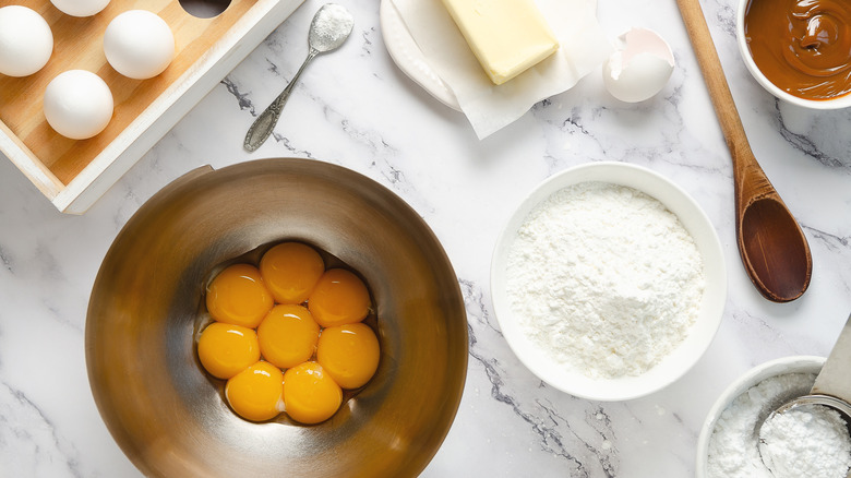 Egg yolks and baking ingredients in bowls on marble counter