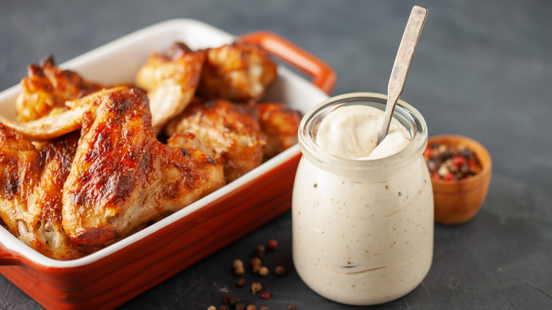 Chicken wings in baking dish with jar of Alabama white sauce