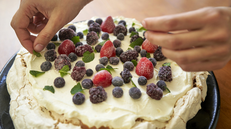Hands placing ingredients on a Pavlova