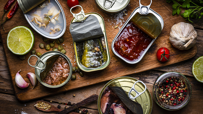 Cans opened on a wooden cutting board surrounded by other foods like garlic, tomato, and peppers