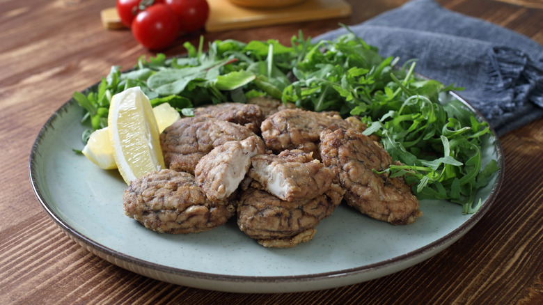 Cooked pork brains on a plate with a bed of greens and a sliced lemon