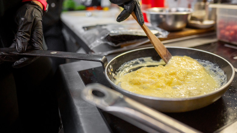 a chef preparing creamy scrambled eggs in a pan with a wooden spatula