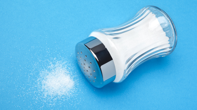 A fallen salt shaker and some salt spilled on the table