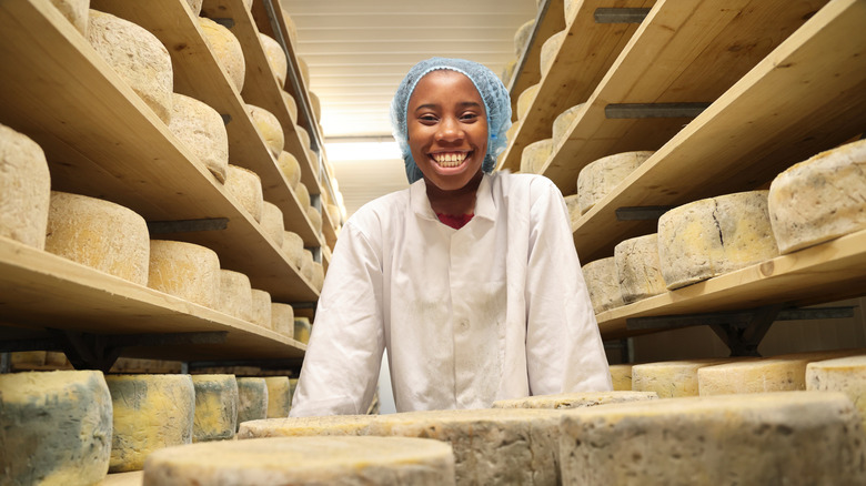 Smiling cheese factory worker surrounded by cheese wheels