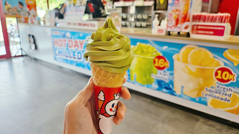 Hand holds green ice cream cone inside fast food joint