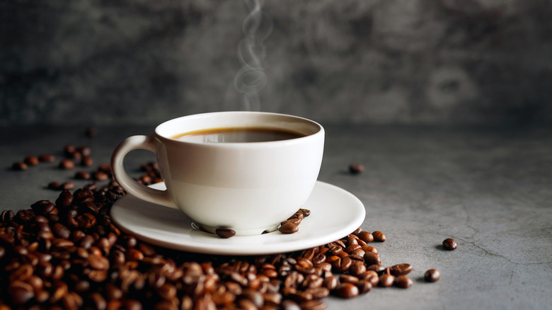 A steaming cup of coffee surrounded by coffee beans