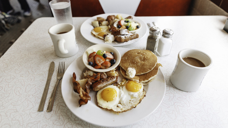 A typical diner breakfast sits on a white table with a red booth chair in the background