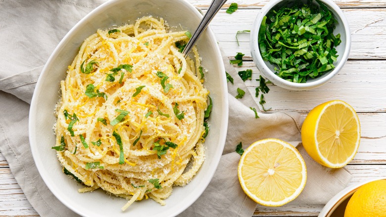 Top-down view of a bowl of pasta next to lemons and herbs