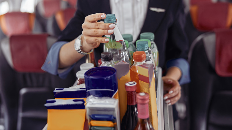 Stewardess grabbing water bottle from drink cart on airplane