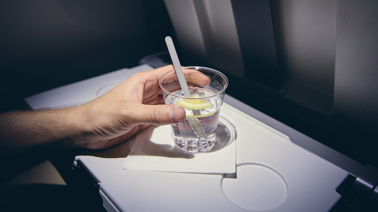 A hand holding a gin and tonic in a plastic cup on an airplane seat tray