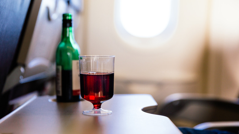 A small plastic cup of red wine on an airplane seat tray
