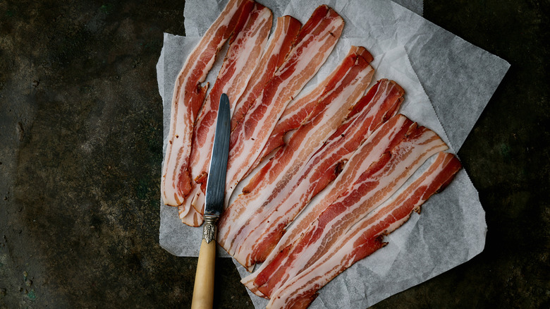 Raw strips of bacon laid on parchment paper with a butter knife