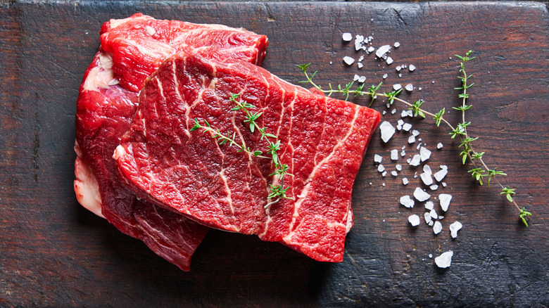 Lean steaks of beef on a wooden board with sea salt and thyme on the side