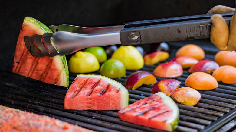 A person grilling sliced watermelons, peaches and lemons on a grill