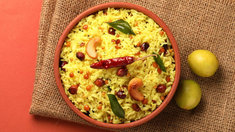 A bowl of yellow rice garnished with red peppers and their small green leaves