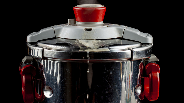 A pressure cooker giving off steam, with a starchy white foam exiting a valve
