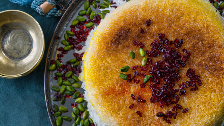 A plate of crispy browned rice garnished with pistachios and pomegranate seeds