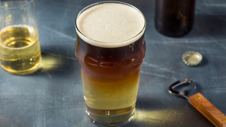 A traditional snakebite beer cocktail in a pint glass, with lighter liquid on the bottom and darker liquid on the top