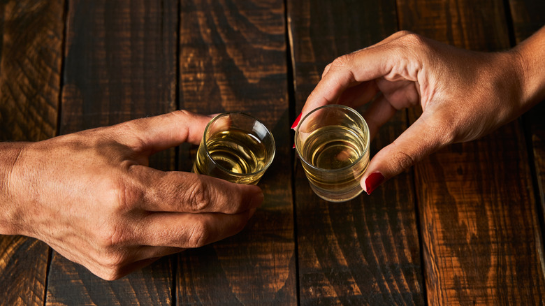 Two hands toasting shot glasses with amber liquid