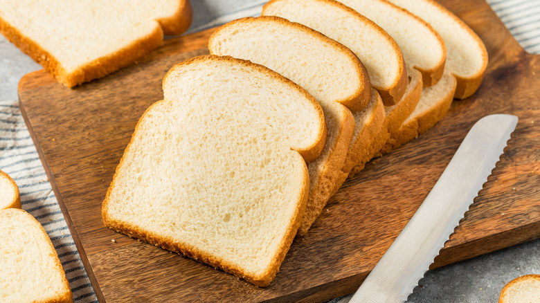 Sliced white bread on wooden cutting board by knife