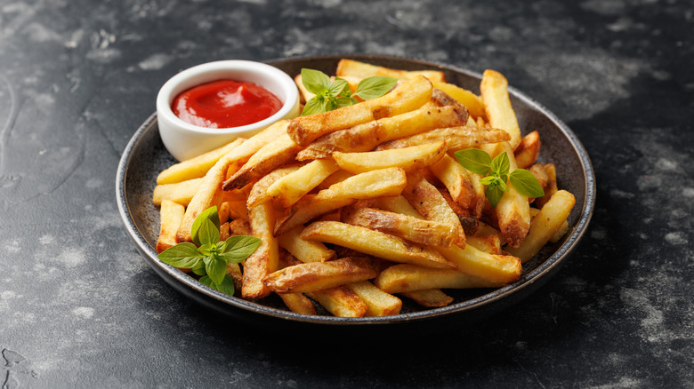 Homemade french fries with ketchup and garnish in black plate on dark background