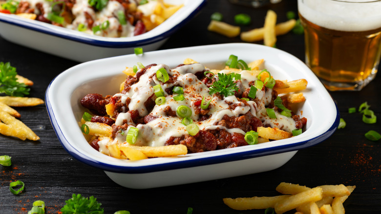 Chili cheese fries on a black wooden table with beer in the background