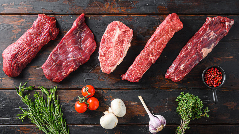 Variety cuts of raw steak with herbs and peppercorns