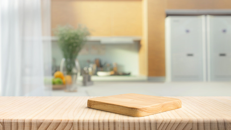 Cutting board on empty countertop with kitchen in backdrop
