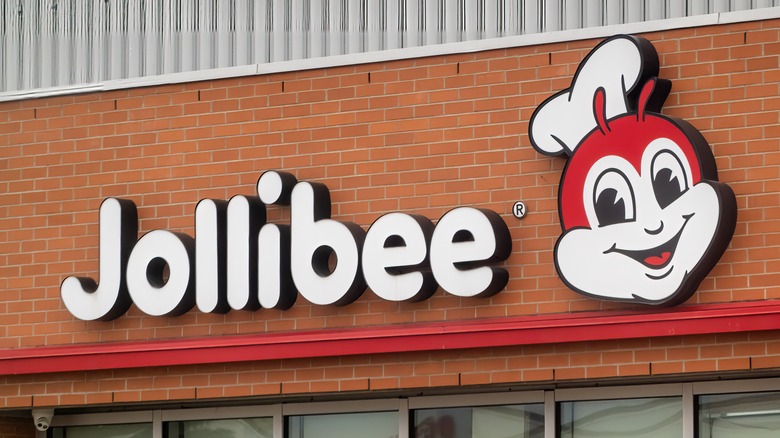 An exterior Jollibee sign, with the name in rounded white text, and the restaurant's smiling bee logo wearing a chef's hat