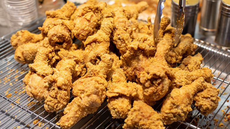 A stainless steel tray in a restaurant kitchen, piled high with pieces of fried chicken