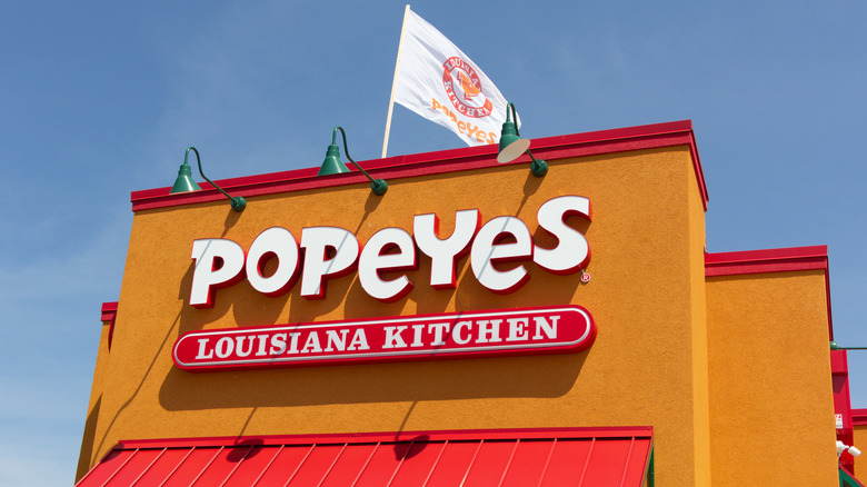 The outside of a standalone Popeyes Louisiana Kitchen, with orange walls, red awning and ceiling trip, and a white and orange Popeyes flag