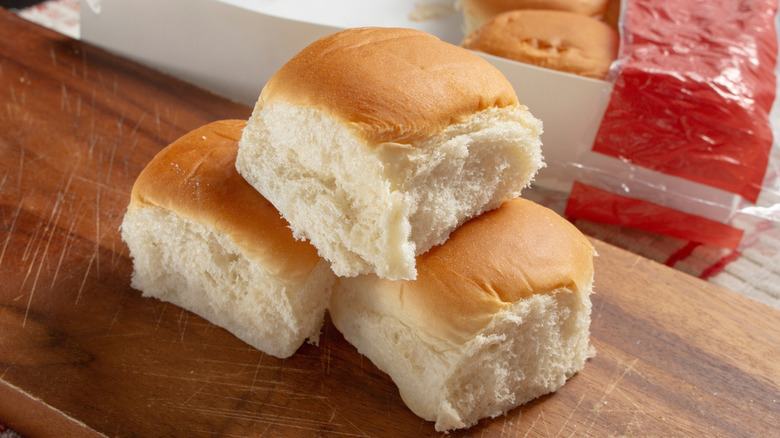 Three King's Hawaiian sweet bread rolls stacked on a table next to the package