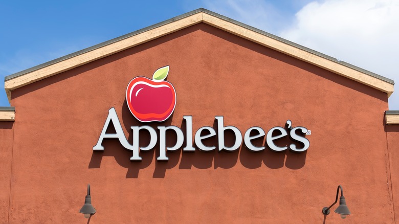 An Applebee's logo sign on a medium brown wall with a farmhouse-style roofline against a blue sky
