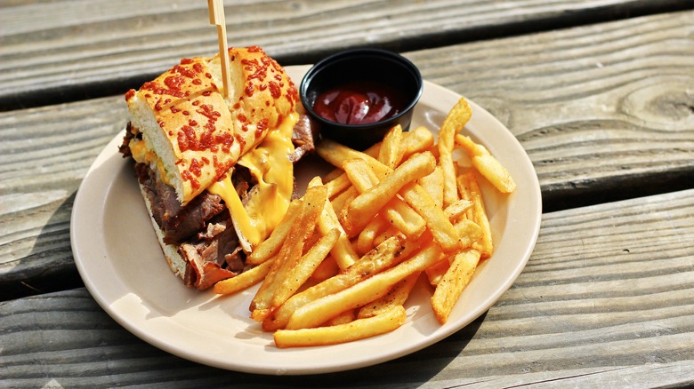 Half a sandwich with prime rib, several yellow cheeses, and a cheese bun, with a side of french fries and a small black cup of ketchup