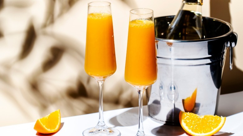 Two Mimosas next to a bottle of chilled Champagne in a bucket
