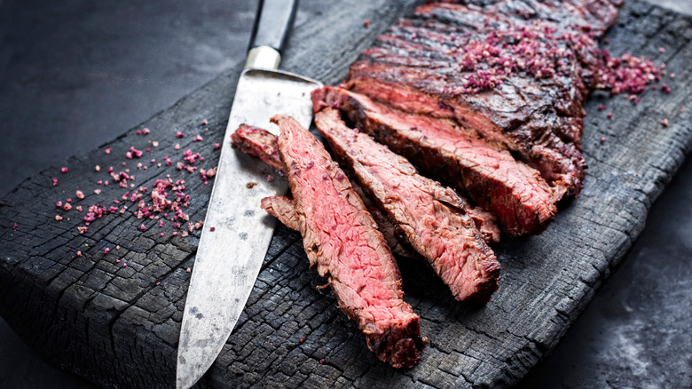 Sliced flap steak with knife on piece of charred wood