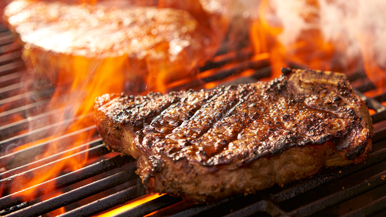 Ribeye steaks cooking on a flaming grill