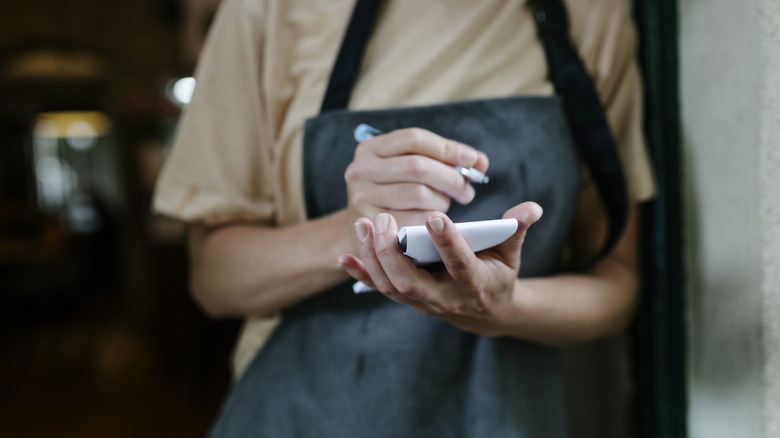Restaurant server's hands holding a pen and pad