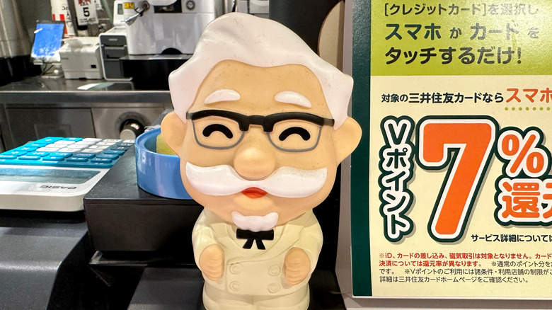 A small, kawaii-style statuette of Colonel Sanders next to the cash register at a Japanese KFC restaurant