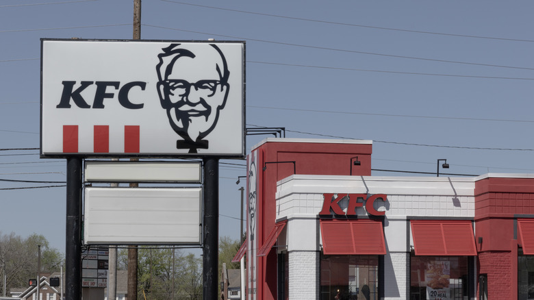 A modern KFC store with a black and white sign featuring Colonel Sanders' likeness and three red stripes below "KFC"