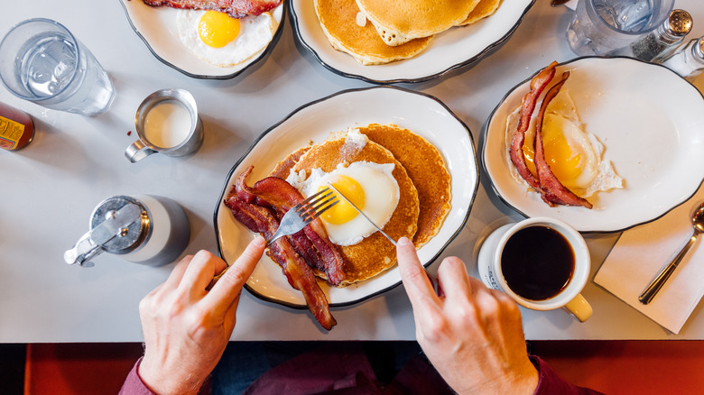 Person eating pancakes, eggs, and bacon in diner